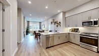 This thoughtfully designed single-floor residence offers a seamless open-concept layout that connects the kitchen, dining, and living areas into one cohesive, light-filled space. The kitchen is appointed with grey shaker-style cabinetry, gleaming white quartz countertops, a large peninsula with seating, stainless steel appliances, a subway tile backsplash, and a built-in wine rack — providing both style and function. Light hardwood flooring flows throughout, lending warmth and continuity across all areas. The dining area sits adjacent to the kitchen and is accented by a striking gallery-style wall display, while the living room offers a comfortable retreat with neutral tones and generous natural light. Two well-appointed bedrooms feature large windows with urban views, soft drapery, and ample space. The primary bathroom includes a glass-enclosed walk-in shower, stone-look tile flooring, and taupe cabinetry with a white vanity top. A secondary half bath mirrors the cohesive design palette. A dedicated study provides a quiet, functional workspace complete with built-in shelving. Recessed lighting throughout enhances the clean, contemporary aesthetic of the entire space.