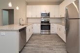 This single-floor residence is designed with a clean, contemporary aesthetic that prioritizes both functionality and comfort. The kitchen serves as a central highlight, featuring full-height white shaker cabinetry, a subway tile backsplash, granite countertops, and a complete suite of stainless steel appliances including a range, microwave, dishwasher, and refrigerator. A peninsula with an undermount sink and pendant lighting adds both workspace and visual interest, while wood-look luxury vinyl flooring ties the space together seamlessly.

The bedrooms are finished with plush wall-to-wall carpeting and feature windows with blinds that invite natural light and offer views of surrounding greenery. Ceiling fans provide additional comfort in the sleeping areas. The primary suite connects directly to a well-sized walk-in closet outfitted with wire shelving, as well as a private bathroom featuring a granite-topped vanity and a tub-shower combination with white subway tile surround. A secondary full bathroom mirrors this refined finish quality. Common areas display the same wood-look flooring found in the kitchen, maintaining a cohesive, neutral palette throughout the residence.