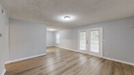 Located at 3954 Memorial College Ave in Clarkston, GA, this well-appointed 2-bedroom, 1-bathroom single-story home offers a thoughtfully designed layout with consistent hardwood-style flooring throughout. The open living and dining area is bright and welcoming, featuring neutral light-gray walls, a textured ceiling, and a standout set of French doors that invite natural light and provide access to the outdoors. A separate entry area includes a louvered closet door, providing convenient storage near the front entrance. The kitchen is efficiently laid out with bold dark cabinetry, white countertops, and a full suite of stainless steel appliances including a refrigerator, electric range, and dishwasher — combining style with function. Both bedrooms are comfortably sized, filled with natural light from windows overlooking greenery, and feature the same warm flooring found throughout the home. The primary bedroom includes a spacious closet with built-in hanging rods. The full bathroom is clean and functional, offering a tub/shower combination, a dark-framed vanity with white countertop, and matching flooring. Two hallways and two closets further enhance the home's storage and flow.