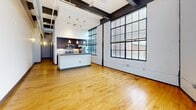 Located in the heart of downtown Winston-Salem, this loft-style unit at 101 E Sixth St blends industrial character with modern finishes. The open living area showcases soaring ceilings with exposed beams and ductwork, warm hardwood floors, and dramatic floor-to-ceiling grid windows that flood the space with natural light and offer views of the surrounding brick streetscape. The kitchen features dark cabinetry, stainless steel appliances, pendant lighting, and an island. Both bedrooms offer hardwood floors, high ceilings, and generous closet space with bifold doors. Each bathroom is finished with tile flooring, a tub-shower combo, and dark wood vanities with granite countertops.
