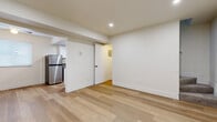 This two-floor space offers a clean, modern aesthetic achieved through thoughtful updates and a consistent neutral palette. The lower level features light hardwood-style flooring that runs throughout the main living and kitchen areas, contributing to a bright and cohesive feel. Recessed lighting illuminates the open living space, which includes baseboard heating and direct access to the exterior entry door, framed by a window that allows natural light inside. The galley-style kitchen is well-appointed with white shaker cabinetry, grey countertops, stainless steel appliances including a full-sized refrigerator, gas range, and built-in microwave, all set against light hardwood-style flooring. The bathroom has been renovated with large-format white wall tiles surrounding the soaking tub and shower, complemented by matte black fixtures and hardware, with a small window providing ventilation. The upper level houses the bedrooms, each carpeted and finished with crisp white walls, sliding closet doors with interior shelving, baseboard heating, and windows that bring in natural light and exterior views. The overall ambiance across both floors is clean, minimal, and move-in ready.