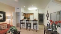 This two-story residence offers a thoughtfully designed layout that blends comfort and functionality across both levels. The heart of the home is an open-concept kitchen and living area, where a raised breakfast bar with seating for three serves as a natural gathering point. The kitchen is equipped with warm honey-toned cabinetry, a full-size refrigerator, and a skylight-style overhead fixture that keeps the space bright and welcoming. Recessed lighting throughout adds a polished finish to the clean, white walls and ceilings.

The living area features plush wall-to-wall carpeting that creates a cozy, inviting atmosphere, while tile flooring in the kitchen and adjoining areas provides a practical and durable surface. A glimpse into the adjacent spaces reveals a spacious walk-in closet with built-in shelving, offering generous storage. Doorways leading to additional rooms suggest a well-distributed floor plan that accommodates both everyday living and private retreat. The overall ambiance is light, neutral, and move-in ready, with a cohesive design aesthetic that makes the space feel both polished and livable across its two floors.