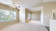 Located at 10840 State Bridge Rd in Alpharetta, Georgia, this single-floor residence offers a well-organized layout with a consistent neutral color palette and practical finishes throughout. The open living and dining area is a standout feature, showcasing vaulted ceilings, soft carpeting, and natural light streaming in through multiple windows with slatted blinds. A ceiling fan with integrated lighting anchors the living space, while track lighting illuminates the adjoining dining area. French-style doors provide additional light and a connection to the outdoors. The galley-style kitchen is equipped with dark cabinetry, granite-style countertops, stainless steel appliances including a refrigerator, electric range, and built-in microwave, and wood-look flooring that adds warmth and durability. The bedrooms are generously sized, each featuring plush carpeting, large windows with outdoor views of surrounding greenery, and ceiling fans for comfort. One bedroom benefits from a vaulted ceiling detail that adds a sense of openness. The bathroom includes a tiled tub-shower combination and granite-topped vanity. Throughout the residence, clean white trim, neutral beige walls, and an airy layout contribute to a bright and welcoming atmosphere.