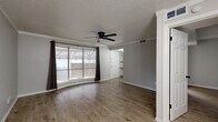 Located at 13980 Peyton Drive in Dallas, TX, this single-story, one-bedroom, two-bathroom home offers a thoughtfully designed layout that maximizes every square foot of its compact footprint. The combined living and dining area serves as the heart of the home, featuring warm wood-look flooring, crown molding, a textured ceiling, and a ceiling fan. A large curved bay window floods the space with natural light and offers views of the covered outdoor area, while dark curtains provide privacy and contrast. The living area flows naturally into the dining space, which is illuminated by a chandelier and opens to the kitchen via a pass-through counter. The kitchen is equipped with gray cabinetry, a coil-burner electric range, an over-range vent hood, and a pantry for additional storage. The generously sized bedroom includes two closets, a ceiling fan, and a window for natural light. Two full bathrooms serve the home — the primary bath features gray shaker-style cabinetry, a white quartz countertop, black hardware accents, and wood-look flooring with shiplap wall detailing. A dedicated laundry area and additional closet storage round out the functional amenities of this efficiently organized Dallas home.