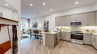 This thoughtfully designed single-floor residence offers a seamless blend of modern aesthetics and functional living. The open-concept layout connects the kitchen, dining, and living areas into one cohesive, light-filled space. The kitchen is outfitted with gray shaker-style cabinetry, stainless steel appliances including a French door refrigerator with a built-in wine rack above, quartz countertops, a subway tile backsplash, and a peninsula with bar seating. Adjacent to the kitchen, the dining area provides an intimate setting, while the living room benefits from large windows that invite natural light and views of the surrounding neighborhood. Light-toned hardwood flooring flows throughout the entire residence, reinforcing a clean, contemporary feel. The primary bedroom is a calm retreat with large windows, a walk-in closet with built-in shelving, and easy access to the spa-inspired bathroom, which features a full glass-enclosed walk-in shower with floor-to-ceiling tile, a handheld showerhead, and a sleek vanity. A second bedroom offers comfortable accommodations, complemented by a dedicated home office nook complete with built-in wall shelving — ideal for remote work or study. Recessed lighting throughout adds to the bright, polished ambiance of this well-appointed residence.