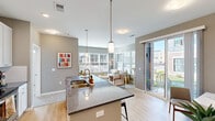 Located in West Chester, Ohio, this single-floor residence offers a thoughtfully designed open-concept layout with modern finishes throughout. The kitchen serves as the centerpiece of the living space, featuring crisp white shaker cabinetry, granite countertops, a large island with bar seating and an undermount sink, and a full suite of stainless steel appliances including a refrigerator, range, and built-in microwave. Pendant lighting illuminates the island, adding a contemporary touch. Light hardwood flooring flows through the kitchen and into the connected dining and living areas, where expansive windows with horizontal blinds invite abundant natural light and provide views of the surrounding neighborhood. A sliding glass door opens to an outdoor patio, extending the living space outward. The living room is generously sized with plush carpet and large corner windows that create a bright, airy atmosphere. Two well-appointed bedrooms offer comfortable retreats, each with carpeted floors, neutral tones, and windows with outdoor views. The primary bathroom features a dual-sink granite vanity with white cabinetry and a large mirror, while a second bathroom includes a full tub-shower combination. The space combines clean architectural lines with warm, welcoming interiors throughout.