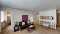 Located in the Quadrangle community of Carbondale, IL, this single-floor unit offers a practical and comfortable layout well-suited for everyday living. The living room serves as the central gathering space, featuring wall-to-wall carpeting, painted cinder block walls, and a textured ceiling. A pass-through opening connects the living area to the kitchen, creating an open sightline and enhancing the sense of space. A compact dining area with a bistro-style table sits adjacent to the pass-through, making use of natural light from a nearby window. The kitchen is equipped with a white electric range, ample upper cabinetry in a light sage tone, and generous counter space for meal preparation. A dedicated bedroom provides a quiet retreat with carpeted flooring, a cinder block accent wall, a large window that brings in natural light, and a wall-mounted HVAC unit for personalized climate control. An open clothing rack offers convenient storage within the room. The full bathroom includes a single-sink vanity with a wide mirror, a tub-shower combination, and tiled walls. Throughout the unit, the straightforward design and functional features provide a solid foundation for comfortable, practical living in Carbondale.