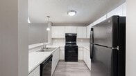 Located at 2600 Colonial Towers Dr in Memphis, Tennessee, this two-bedroom, two-bathroom residence offers a thoughtfully laid-out single-floor plan with a clean, neutral aesthetic throughout. The kitchen is a standout feature, boasting a U-shaped design with white cabinetry providing ample storage, light-toned countertops, and a full suite of black appliances including a gas range and stainless steel refrigerator. Pendant lighting and wood-look flooring add a modern touch to this functional space. The open living room is bright and inviting, featuring wood-look flooring, soft neutral walls, a textured ceiling, and a sliding glass door that floods the room with natural light and provides access to an outdoor view of surrounding trees. The spacious primary bedroom features plush carpeting, vertical blinds over a sliding glass door, and generous proportions that offer a comfortable retreat. The second bedroom is equally well-appointed with carpet flooring and easy access to the hallway. Both bathrooms are finished with wood-look flooring and include a tub-shower combination. A connecting hallway ties the layout together seamlessly, making this a practical and comfortable home in the Memphis area.