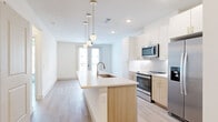 This thoughtfully designed single-floor residence offers a bright, open layout with a clean modern aesthetic. Light wood-tone flooring flows consistently throughout, tying each space together cohesively.

The kitchen serves as the centerpiece of the main living area, anchored by a generous island with a white quartz countertop, an undermount sink, and warm natural wood cabinetry accented with gold hardware. Stylish globe pendant lights hang above the island, adding a contemporary touch. The kitchen is equipped with stainless steel appliances, including a range, microwave, and refrigerator, complemented by white upper cabinetry and a classic subway tile backsplash. In-unit side-by-side washer and dryer units are conveniently tucked nearby. A glass door at the far end of the space fills the open living area with natural light.

The bedroom is a calm, well-proportioned retreat featuring light-toned walls, light wood flooring, a ceiling fan, and a large window that invites ample natural light and views of the surrounding neighborhood.

The bathroom offers a clean, spa-like atmosphere with large-format tile flooring, a glass-enclosed walk-in shower with subway tile surround and a built-in niche, a wood-toned vanity, and direct access to a dedicated walk-in closet complete with built-in shelving and hanging rods.
