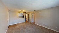 This single-story 1-bedroom, 1-bathroom unit in Long Beach, Mississippi offers a practical and comfortable layout designed for easy living. The living area is carpeted and bright, featuring a ceiling fan with light fixture and French doors fitted with blinds that allow natural light to filter in while providing privacy. A pass-through opening connects the living space to the kitchen, creating an open and communicative feel between the two areas. The kitchen is equipped with gray shaker-style cabinetry, granite-style countertops, a black electric range with overhead ventilation, and a built-in refrigerator, providing a functional cooking environment. The bedroom is a well-proportioned, carpeted room with a ceiling fan, a window with blinds for natural light, and built-in shelving for additional storage. A closet and a floor-level HVAC vent add to the room's functionality. The bathroom features wood-look flooring, white shaker cabinetry topped with granite-style counters, an undermount sink with brushed nickel fixtures, and a separate shower stall with a clean white surround. Neutral wall tones and textured ceilings are consistent throughout, lending the space a cohesive and well-maintained aesthetic.