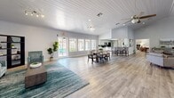 Located at 4201 W Rochelle Ave in Las Vegas, NV, this expansive single-floor community space offers a generous, open layout designed for comfort and versatility. The interior is anchored by two distinct living areas, both finished with light-toned hardwood-style flooring that extends seamlessly throughout the space.

The main living area is a standout, featuring soaring vaulted ceilings clad in white shiplap, recessed lighting, and dual ceiling fans. A dramatic floor-to-ceiling mosaic tile fireplace serves as the focal point, flanked by large windows that flood the room with natural light and offer views of the surrounding greenery. Multiple seating arrangements make this area ideal for both gathering and relaxation.

A second, more intimate living area provides a quieter setting, complete with vaulted ceilings, wainscoting, and windows overlooking the outdoors. This zone also accommodates a desk workspace, adding functional versatility.

The space further includes an open dining area with a full table and seating, directly adjacent to a well-equipped kitchen featuring a breakfast bar with counter-height seating, modern appliances, and a pass-through counter. Additional lounge nooks with contemporary furnishings round out the layout, making this a well-appointed, multi-functional gathering facility.