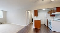 This single-floor unit offers a practical and well-organized layout designed for comfortable everyday living. The living area combines hardwood-style flooring with plush carpeting, creating a natural transition between zones. A large window allows natural light to fill the space, complemented by a ceiling fan overhead. A wall-mounted air conditioning unit and baseboard heater provide year-round climate control.

The galley-style kitchen is efficiently arranged, featuring warm medium-toned wood cabinetry on both sides, light marble-look countertops, a double stainless steel sink, a white electric range with overhead ventilation, and a full-size refrigerator. The kitchen opens toward the main living space, enhancing the sense of connectivity throughout the unit.

The bedrooms are carpeted and neutrally finished, with one room offering full-length mirrored sliding closet doors that add visual depth. Each room provides a clean, versatile canvas suited to a variety of furniture arrangements.

The bathroom is finished with a wide dark-toned vanity, white countertop, large mirror, and a tiled tub-shower combination. Textured tile flooring adds a classic touch. Throughout the unit, textured ceilings, neutral walls, and consistent finishes contribute to a cohesive, understated aesthetic.