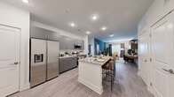 This thoughtfully designed 2-bedroom, 3-bathroom residence features a contemporary open-concept layout that seamlessly connects the kitchen, dining, and living areas. The kitchen is equipped with stainless steel appliances, sleek gray cabinetry, granite countertops, and a central island with bar seating and an integrated sink — ideal for both meal preparation and casual dining. Wood-style flooring flows throughout the main living spaces, complementing the clean, modern aesthetic.

The living room features a striking blue accent wall, large windows that invite natural light, and ample space for comfortable seating arrangements. The primary bedroom continues the blue accent wall motif and includes generous closet space complete with wire shelving systems for organized storage. The second bedroom is equally well-appointed with its own closet access.

Three full bathrooms serve the residence, each finished with granite-topped gray vanities and wood-style flooring. The bathrooms are notable for their elongated layouts, providing functional space and direct access to the adjoining closets. Two dedicated closets add to the overall storage capacity of the unit.

Throughout the residence, recessed lighting, neutral wall tones, and consistent high-quality finishes create a cohesive and inviting atmosphere suited for modern living.