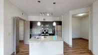 This single-story, one-bedroom, one-bathroom unit offers a well-designed open-concept layout with contemporary finishes throughout. The living area is anchored by warm wood-style flooring, a ceiling fan, and a sliding glass door that opens to a private balcony with outdoor views, allowing natural light to flow freely into the space.

The kitchen is a standout feature, showcasing dark espresso cabinetry, a mosaic tile backsplash, granite countertops, and a large central island with an undermount sink. Stainless steel appliances—including a refrigerator, range, and built-in microwave—are complemented by sleek pendant lighting and a track light fixture overhead, creating a polished, functional workspace ideal for cooking and entertaining.

The bedroom features plush carpet flooring, multiple windows with blinds, and a ceiling fan, providing a comfortable and well-lit retreat. The bathroom includes wood-style flooring, a full soaking tub with white subway tile surround accented by decorative mosaic inlays, dark vanity cabinetry, and granite countertops. A dedicated in-unit laundry area with a full-size washer and dryer adds everyday convenience to this thoughtfully appointed home.