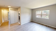 This single-floor residence at 5452 Newton St in Bladensburg, MD offers a clean, updated interior with a neutral color palette and practical layout. The main living area is spacious and open, finished with light hardwood-style flooring and soft gray walls that create a bright, welcoming atmosphere. A large window in this space allows ample natural light to flow in while offering views of the surrounding neighborhood.

The kitchen is well-appointed with white cabinetry accented by matte black hardware, granite countertops featuring a classic white and gray pattern, a stainless steel sink with a black pull-down faucet, and a stainless steel gas range beneath a mounted range hood. The cabinetry provides generous storage, and the overall design is modern yet functional.

A bedroom is carpeted and benefits from dual corner windows that provide cross-ventilation and abundant natural light, with views of the tree-lined surroundings. A separate room with hardwood-style flooring includes a double-door closet and direct visual access to the kitchen area.

The bathroom features a full tub-shower combination with white tile surround, a window for natural light, and a vanity with a white cabinet base. Throughout the unit, consistent finishes and clean lines contribute to a cohesive, move-in ready environment.
