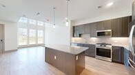 Located at 12455 Eldorado Parkway in Frisco, TX, this contemporary three-story home offers a well-designed layout across three distinct levels. The ground floor provides an entry foyer bathed in natural light through large windows, a garage, and utility spaces. The main living level features an open-concept dining, kitchen, and living area finished with light hardwood flooring throughout. The gourmet kitchen is a standout, boasting dark wood cabinetry, granite countertops, a subway tile backsplash, a central island with pendant lighting, and a full suite of stainless steel appliances. The upper floors house three bedrooms, including a generously sized primary bedroom with a ceiling fan, multiple windows offering neighborhood views, and access to a well-appointed en-suite bathroom featuring dual granite-topped vanities, large-format tile flooring, and a soaking tub with full tile surround. Two loft spaces add flexible living options throughout the home. Eight closets, including walk-in closets with built-in shelving systems, provide ample storage. Five bathrooms, a dedicated laundry room, and three staircases complete this thoughtfully designed home.