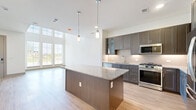 Located at 12455 Eldorado Parkway in Frisco, TX, this contemporary three-story home offers a well-designed layout across three distinct levels. The ground floor provides an entry foyer bathed in natural light through large windows, a garage, and utility spaces. The main living level features an open-concept dining, kitchen, and living area finished with light hardwood flooring throughout. The gourmet kitchen is a standout, boasting dark wood cabinetry, granite countertops, a subway tile backsplash, a central island with pendant lighting, and a full suite of stainless steel appliances. The upper floors house three bedrooms, including a generously sized primary bedroom with a ceiling fan, multiple windows offering neighborhood views, and access to a well-appointed en-suite bathroom featuring dual granite-topped vanities, large-format tile flooring, and a soaking tub with full tile surround. Two loft spaces add flexible living options throughout the home. Eight closets, including walk-in closets with built-in shelving systems, provide ample storage. Five bathrooms, a dedicated laundry room, and three staircases complete this thoughtfully designed home.