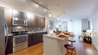 This thoughtfully designed single-floor residence offers a seamless blend of modern style and functional living. The open-concept kitchen serves as the heart of the home, showcasing rich dark espresso cabinetry, granite countertops, a mosaic tile backsplash, and a full suite of stainless steel appliances including a French door refrigerator, range, microwave, and dishwasher. A central island with bar seating and pendant lighting overhead makes the kitchen ideal for both casual dining and entertaining. Warm hardwood flooring flows throughout the main living areas, connecting the kitchen to a comfortable living room featuring a ceiling fan and large sliding door with vertical blinds that invite natural light. The primary bedroom is generously sized, complete with a ceiling fan, a walk-in closet, and direct access to an en suite bathroom. The bathroom is outfitted with a deep soaking tub, large-format tile surround, and a dark vanity topped with granite. A second bedroom, carpeted for comfort, receives abundant natural light through a wide window. The layout also includes a versatile flex space near the entry, well-suited as a sitting area or home office. Track lighting and pendant fixtures throughout enhance the contemporary aesthetic of this well-appointed residence.