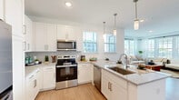 Located at 1700 Ranch Rd. in Nokomis, FL, this well-appointed 2-bedroom, 2-bathroom residence offers a thoughtfully designed single-floor layout that maximizes comfort and functionality. The open-concept living, dining, and kitchen area serves as the heart of the home, filled with natural light streaming through large windows dressed with sheer white curtains and plantation shutters. Light wood-look flooring flows throughout the main living areas, creating a warm, cohesive aesthetic.

The modern kitchen is a standout feature, showcasing white shaker cabinetry, granite countertops, a subway tile backsplash, stainless steel appliances, and a large center island with seating for three — ideal for casual dining. Stylish pendant lighting adds a polished finishing touch. A dedicated pantry provides additional storage convenience.

Both bedrooms are generously proportioned, featuring plush carpeting, ceiling fans, and large windows that invite natural light. The bathrooms are finished with granite vanities, white cabinetry, and a glass-enclosed walk-in shower. Additional highlights include multiple closets, a hallway connecting the private areas, and an in-unit laundry room with side-by-side washer and dryer. This residence combines modern finishes with a clean, airy design throughout.