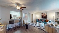 This single-floor residence offers a thoughtfully designed layout that seamlessly connects the main living areas. The open-concept living room is anchored by rich hardwood-style flooring, a ceiling fan with light fixture, and a textured ceiling. A bold teal sofa, geometric-patterned area rug, and curated wall art give the space a vibrant, modern aesthetic. The dining area flows naturally from the living room, featuring a round table with sculpted seating and a large window draped in sheer curtains that invite natural light.

The kitchen is efficiently arranged with white cabinetry extending to the ceiling, granite-style countertops, a stainless steel refrigerator, and a stainless steel sink. A breakfast bar with bar seating connects the kitchen to the living area, creating a convenient and social layout.

The bathroom is clean and functional, outfitted with a tub-shower combination, a wide vanity mirror, and white cabinetry with granite-style countertops. Wood-style flooring carries through for a cohesive finish.

Both bedrooms are carpeted and feature textured ceilings. The primary bedroom is generously sized with a large window and a herringbone-style wooden bed frame and matching dresser. The second bedroom offers a cozy, well-lit atmosphere with twin bedside lamps and warm, neutral tones throughout.