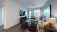 This thoughtfully designed single-floor residence offers a cohesive blend of modern finishes and functional living spaces. The kitchen stands out with crisp white shaker cabinetry extending to the ceiling, granite countertops, a subway tile backsplash, stainless steel appliances including a French door refrigerator and range, and a large central island topped with pendant lighting — ideal for both cooking and casual dining. Rich hardwood-style flooring runs throughout the main living areas, anchoring the open-concept layout. The living room is bright and welcoming, featuring large windows with decorative drapery that invite natural light, a ceiling fan, and a bold accent wall that lends the space a contemporary character. The primary bathroom offers a long vanity with granite countertops, a glass-enclosed walk-in shower, and light-toned tile flooring. A second full bathroom mirrors the refined aesthetic with a granite vanity, soaking tub with shower, and clean tile flooring. The bedroom features generous windows with views of lush outdoor greenery, dark hardwood floors, and a serene, restful ambiance. A dedicated laundry area with a full-size top-loading washer and dryer and built-in shelving adds practical convenience to this well-rounded residence.