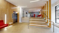 Located at 65 Brainerd Road in Boston's Allston neighborhood, this single-floor communal space serves as the central hub of the building. The grand entrance features floor-to-ceiling glass walls and a wood-paneled vestibule, flooding the interior with natural light and offering clear views of the surrounding streetscape. A striking staircase with wood-faced steps and illuminated risers, paired with sleek glass railings, anchors the architectural design and guides residents seamlessly through the space.

The expansive living area is warmly appointed with hardwood flooring, mid-century modern furnishings in bold red accents, and sheer curtains that diffuse natural light throughout. A built-in media wall with a large flat-screen TV, set against a vibrant red accent wall and flanked by white open shelving, creates a dynamic focal point for relaxation and socializing.

The kitchen is a design standout, featuring bold red sliding panels, a clean white island with bar seating, and stylish pendant lighting that adds warmth and character. Adjacent areas include a mailroom equipped with smart package lockers and individual mailboxes, providing modern convenience. Elevator access and refined recessed linear lighting throughout complete this polished, amenity-rich communal environment.