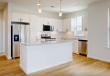 This 1,090-square-foot single-floor residence at 770 Collins Hill Rd in Lawrenceville, GA offers a clean, modern aesthetic with consistent finishes throughout. The open-concept kitchen and living area serves as the heart of the home, featuring white shaker cabinetry with matte black hardware, granite countertops, a white subway tile backsplash, and a central island. Stainless steel appliances include a Whirlpool range, over-the-range microwave, refrigerator, and dishwasher. Light hardwood flooring flows through the main living areas, complemented by an abundance of natural light from multiple windows with blinds and a glass-panel exterior door. The two bedrooms are carpeted and equipped with ceiling fans; the primary bedroom spans 160 square feet and features a double-door closet, while the secondary bedroom includes a walk-in closet. Both bathrooms maintain the home's cohesive design with granite-topped white vanities and hardwood-style flooring. One bathroom offers a glass-enclosed walk-in shower with white tile surround, while the second features a tiled tub-shower combo. A dedicated laundry room houses a full-size Whirlpool washer and dryer with overhead shelving, adding practical convenience to this well-appointed home.