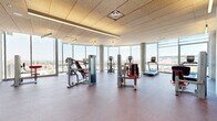 Located in the heart of Phoenix at 440 E Van Buren St, this generously sized fitness center occupies a single floor and offers a comprehensive, well-appointed exercise facility. The space is defined by its dramatic floor-to-ceiling curtain-wall windows that wrap around much of the perimeter, flooding the interior with natural light and providing panoramic views of the Phoenix skyline and surrounding cityscape — a standout feature that elevates the workout experience.

The main exercise area is outfitted with a robust selection of Matrix-branded strength training machines, including cable systems, resistance machines, and adjustable benches, alongside free weights and a dumbbell rack. Cardio equipment — treadmills, stationary bikes, and elliptical trainers — is positioned along the window line, allowing users to take in the city views during their workouts. Durable rubber flooring covers the primary training zones, while large-format tile flooring delineates designated stretching and functional training areas.

A separate multipurpose studio room features smooth hardwood flooring, a wall-mounted flat-screen television, and direct access to an outdoor terrace, making it well-suited for group fitness classes or yoga. Additional amenities include mounted TVs throughout, water stations, and clearly marked entry and exit points. The textured drop ceiling with integrated linear lighting lends a modern, polished aesthetic throughout the entire facility.