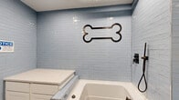 Located at 4247 Locust St in Philadelphia, PA, this specialized pet grooming facility is part of the Fairfax building and is thoughtfully designed to accommodate pet care needs. The space consists of a grooming bathroom and a connecting hallway, offering a compact yet fully functional layout.

The grooming bathroom is the centerpiece of the space, finished with glossy light blue subway tiles that line the walls from floor to ceiling, creating a clean and bright aesthetic. A deep, built-in pet wash tub with a matte black faucet fixture provides a dedicated bathing station, while a white cabinet unit with a smooth countertop surface offers convenient storage and workspace for grooming supplies. A decorative metal dog bone accent mounted on the tiled wall adds a playful, pet-friendly touch to the room. The floor is finished with light-toned tile, contributing to the hygienic, easy-to-clean environment.

The hallway connecting the grooming room to the rest of the building features polished terrazzo-style flooring, exposed industrial piping along the ceiling, and bright overhead lighting. Light gray walls with crisp white baseboards line the corridor, and a branded Fairfax welcome mat marks the entryway. Signage throughout directs visitors clearly, reinforcing the building's well-organized, amenity-focused character.