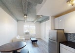 Located on the iconic Collins Avenue in the heart of Miami Beach, this single-floor unit offers a functional and thoughtfully arranged layout. The open-plan living and dining area forms the core of the space, featuring light wood-look flooring and distinctive exposed concrete beams across the textured ceiling, lending an industrial character to the otherwise clean, white interior. A cream leather loveseat, glass-top coffee table, and a round dining table with industrial-style stools complete the living area, which receives natural light through a street-facing window. The kitchen is efficiently designed with white cabinetry, a mosaic tile backsplash, stainless steel refrigerator, and a gas range, making the most of the available footprint. The bedroom is a serene, white-walled retreat with natural light filtering in through a window with neighborhood views, continuing the same exposed beam ceiling detail found throughout. The bathroom is clean and well-appointed, featuring a combination tub and shower, a pedestal vanity with brushed nickel fixtures, and a wall-mounted mirror. Throughout the unit, the consistent use of white walls, light flooring, and natural light creates a bright, cohesive ambiance well-suited to the vibrant Miami Beach surroundings.