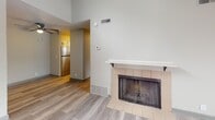 This single-floor unit presents a clean, neutral aesthetic throughout, with light wood-style flooring and soft gray-toned walls creating a cohesive and airy atmosphere. The living area is a notable highlight, featuring vaulted ceilings that add a sense of openness and volume. A tile-surround fireplace with a white mantel serves as a focal point, while a sliding glass door fitted with vertical blinds opens to an outdoor balcony, allowing natural light to fill the space.

The kitchen is thoughtfully appointed with white cabinetry, white countertops, stainless steel appliances including a refrigerator and electric range, and a striking multicolored stone tile backsplash that introduces warmth and texture to the otherwise neutral palette.

The bedrooms are comfortably sized, each featuring wood-style flooring, textured ceilings, and windows with blinds that bring in ample natural light. The bathroom includes a white vanity with a single-basin sink, a tri-light bar fixture with dark hardware accents, and a separate water closet with a full tub and shower combination, providing a practical and well-organized layout throughout.