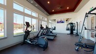Located at 575 Concord Rd in Jefferson, GA, this fitness center offers a thoughtfully designed single-floor workout facility that balances functionality with an inviting atmosphere. The space is defined by its striking tray ceiling finished in a rich, dark red tone and accented with recessed lighting and a ceiling fan, creating a polished yet energetic ambiance throughout.

Large, floor-to-ceiling windows line the walls, flooding the interior with abundant natural light and offering direct views of the outdoor pool area and surrounding pergola, making workouts feel open and refreshing. Full-length mirrors are strategically placed to amplify the sense of space and allow users to monitor their form during exercise.

The cardio zone is comprehensively outfitted with treadmills, ellipticals, stationary bikes, and rowing machines — including Precor equipment — all positioned to take advantage of the exterior views. A flat-screen television is wall-mounted for entertainment during sessions.

The strength training area features a multi-functional cable machine, a Smith machine, adjustable benches, and a well-stocked dumbbell rack, catering to a wide range of resistance training needs. Durable rubber flooring covers the entire space, providing comfort and safety underfoot. The fitness center is accessed through glass-panel doors, reinforcing its bright, transparent aesthetic and seamlessly connecting it to the broader community amenity area.