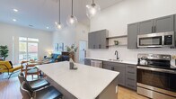 Located at 75 Canal St in Manchester, NH, this well-appointed 2-bedroom, 2-bathroom residence offers a thoughtfully designed single-floor layout with modern finishes throughout. The open-concept kitchen is a standout feature, showcasing gray shaker cabinetry with matte black hardware, crisp white quartz countertops, a full suite of stainless steel appliances, and a generous island with bar seating. Globe pendant lights hang from the soaring ceilings, adding a contemporary touch. The kitchen flows seamlessly into the living area, which benefits from high ceilings and warm hardwood-style flooring, creating an airy and inviting atmosphere. Both bedrooms are carpeted and feature tall ceilings and windows overlooking a natural outdoor setting, filling the rooms with soft, natural light. The primary bedroom offers a comfortable and spacious retreat. Each of the two bathrooms is finished with gray vanity cabinetry, white countertops, matte black fixtures, and wood-look flooring. One bathroom features a tiled walk-in shower, while the other includes a shower-tub combo. Additional spaces include a hallway, entrance, and two closets, providing practical storage solutions. The unit also includes two dedicated closets for added convenience.