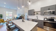 Located at 75 Canal St in Manchester, NH, this well-appointed 2-bedroom, 2-bathroom residence offers a thoughtfully designed single-floor layout with modern finishes throughout. The open-concept kitchen is a standout feature, showcasing gray shaker cabinetry with matte black hardware, crisp white quartz countertops, a full suite of stainless steel appliances, and a generous island with bar seating. Globe pendant lights hang from the soaring ceilings, adding a contemporary touch. The kitchen flows seamlessly into the living area, which benefits from high ceilings and warm hardwood-style flooring, creating an airy and inviting atmosphere. Both bedrooms are carpeted and feature tall ceilings and windows overlooking a natural outdoor setting, filling the rooms with soft, natural light. The primary bedroom offers a comfortable and spacious retreat. Each of the two bathrooms is finished with gray vanity cabinetry, white countertops, matte black fixtures, and wood-look flooring. One bathroom features a tiled walk-in shower, while the other includes a shower-tub combo. Additional spaces include a hallway, entrance, and two closets, providing practical storage solutions. The unit also includes two dedicated closets for added convenience.