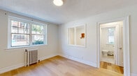 Located in Toronto's charming Queen Street East neighbourhood, this compact one-bedroom, one-bathroom unit offers a practical and efficient layout across a single floor. The living area is bright and welcoming, featuring warm light hardwood flooring throughout and a textured ceiling that adds subtle character. A large double-pane window allows generous natural light to flow into the space, while a classic white cast-iron radiator provides reliable heating. A built-in pass-through window connects the living area to the adjacent space, adding a distinctive architectural detail. The bedroom is an intimate, well-proportioned room with the same hardwood flooring, its own radiator, and a window that frames views of the surrounding greenery, creating a calm and restful atmosphere. The bathroom is finished with neutral large-format floor tiles and is equipped with a pedestal sink, toilet, and bathtub. A frosted window allows natural light while maintaining privacy, and a small radiator ensures warmth. Throughout the unit, clean white walls and bright trim create a fresh, neutral palette. The front entry opens directly into the living space, offering a clean, straightforward flow. Situated steps from Queen Street East's shops, cafés, and transit, this unit suits those seeking a functional and well-located home.
