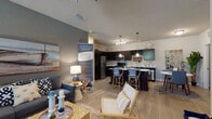 This single-story residence offers a thoughtfully designed open-concept layout that seamlessly connects the living, dining, and kitchen areas. The living room features light wood-style flooring, neutral gray accent walls, and ample space for comfortable furnishings, with natural light filtering through slatted blinds.

The kitchen is a standout feature, showcasing dark espresso cabinetry, stainless steel appliances including a refrigerator, range, and microwave, and striking marble-style countertops that extend to a spacious island with bar seating. A built-in wine rack adds a distinctive touch overhead.

Two well-proportioned bedrooms are finished with plush carpeting and large windows that bring in generous natural light and outdoor greenery views. Each room provides a calm, restful atmosphere with neutral tones and ample wall space.

Two full bathrooms mirror the kitchen's design aesthetic, featuring dark vanity cabinetry, marble-style countertops, wood-look tile flooring, and full tub-shower combinations. The overall interior presents a cohesive modern style with a neutral color palette, durable flooring materials in the main living areas, and consistent finishes throughout.