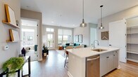 Located in Grandview Heights, Ohio, this thoughtfully designed single-floor residence offers a seamless blend of modern aesthetics and functional living. The open-concept layout connects the kitchen, dining, and living areas into one cohesive, light-filled space. Large windows and roller shades allow abundant natural light throughout, while doors open directly to a private balcony with views of the surrounding neighborhood.

The kitchen is a standout feature, anchored by a generous island with a waterfall-edge countertop, an undermount sink, and seating for multiple guests. Pendant lighting with glass shades illuminates the space, complemented by stainless steel appliances, a stainless refrigerator, and contemporary cabinetry in a soft gray tone.

The living area is bright and welcoming, with wide-plank light hardwood flooring and direct balcony access through a glass-paned door with transom window above. The bedrooms offer plush carpeting, oversized windows with outdoor views, and ample space for furnishings.

Two bathrooms feature large-format tile flooring and white cabinetry with dark hardware. The primary bath includes a glass-enclosed walk-in shower, while the secondary bath offers a tub-shower combination. Neutral warm tones and clean architectural lines tie the entire residence together into a cohesive, modern living environment.