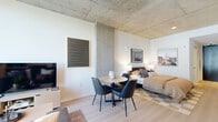 Located at 625 N 2nd Ave in the heart of downtown Phoenix, this modern studio offers a thoughtfully designed open-concept layout that seamlessly integrates the living, dining, and sleeping areas into one efficient, well-appointed space. A defining architectural feature is the exposed concrete ceiling, which lends an industrial-chic character complemented by crisp white walls and light-toned hardwood flooring throughout the main area.

The kitchen is outfitted with full-height dark cabinetry, stainless steel appliances including a French door refrigerator, gas range, dishwasher, and a white subway tile backsplash that adds a clean contrast. The living area flows naturally into the dining space, which features a round table with sleek black chairs, and continues into the sleeping area, all unified under the open ceiling plane. Large windows draw in natural light and offer views of the surrounding cityscape.

A hallway leads to the private bathroom, finished with large-format tile flooring and minimalist black fixtures, maintaining the space's contemporary aesthetic. Additional functional areas include a closet and an in-unit laundry. The overall ambiance is modern and urban, with an industrial warmth that makes this studio a distinctive option in downtown Phoenix.