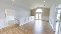 This single-floor, 2-bedroom, 2-bathroom home offers a generous and well-appointed layout designed for comfortable living. The main living area immediately impresses with soaring vaulted ceilings that enhance the sense of openness and volume. Light hardwood-style flooring runs throughout, lending warmth and continuity to the space. Elegant white wainscoting and paneling add a refined architectural detail, creating visual interest along the walls. A striking arched window above a set of French doors floods the room with natural light while framing an inviting view of the outdoors. Recessed lighting is thoughtfully placed throughout the ceiling, providing ample illumination to complement the natural light. The French doors offer direct access to an outdoor area, seamlessly blending indoor and outdoor living. The neutral, earthy wall tones create a calm and versatile backdrop that suits a variety of interior styles. The overall ambiance is bright, airy, and polished, combining classic architectural details with a clean, modern aesthetic that makes this home both functional and visually appealing.