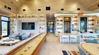 Located at 3573 Oxenfree Blvd in Frisco, TX, this 2,540 sq ft two-story community amenity center spans 1,900 sq ft on the ground floor and 650 sq ft on the upper level. The main floor showcases soaring vaulted ceilings clad in warm wood paneling, creating a bright and welcoming atmosphere throughout. A central clubroom features a shuffleboard table, a gas fireplace framed by a decorative longhorn mount, built-in display shelving, and a large wall-mounted TV — ideal for social gatherings. An adjacent game and lounge area opens through floor-to-ceiling black-framed glass sliding doors to a covered outdoor patio equipped with multiple grills, a long communal dining table, and casual seating. A dedicated fitness center offers cardio machines, air bikes, a full dumbbell rack, and floor-to-ceiling mirrors beneath a vaulted wood ceiling. An outdoor covered sport court provides space for pickleball or basketball, accented by pendant lighting. The surrounding grounds include a manicured green lawn with a playground, pergola shade structure, landscaped walking paths, and a paved upper-level terrace with scenic neighborhood views. The exterior reflects a modern farmhouse aesthetic consistent with the surrounding Frisco community.