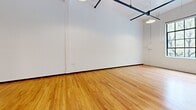 Located at 500 Exposition Ave, Unit 207, this single-floor unit showcases a distinctive industrial-loft aesthetic throughout. The open-concept living and kitchen area is anchored by warm hardwood flooring that extends seamlessly across the entire space, complementing crisp white walls and soaring ceilings. Exposed steel beams, suspended track lighting, and visible ductwork add authentic industrial character overhead, while large, multi-pane steel-framed windows flood the living area with natural light and frame views of surrounding greenery.

The kitchen is thoughtfully appointed with white cabinetry, white countertops, and a full suite of stainless steel appliances, including a refrigerator, electric range, over-the-range microwave, and dishwasher. The layout opens directly to the living area, making the space feel connected and cohesive.

The bathroom features classic white square tile in the tub surround, small-format floor tile, a full bathtub with shower, and a vanity with storage. The clean, neutral palette throughout maintains a consistent and functional aesthetic. Overall, this unit balances industrial design elements with practical living amenities, creating a bright and versatile space.