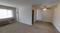 This single-floor residential space presents a clean and functional layout designed for comfortable everyday living. The interior is finished with wall-to-wall carpeting throughout, lending a warm and cohesive feel to the living areas. Neutral, light-toned walls create a bright and open ambiance, maximizing the sense of space across the floor plan.

The main living area is generously proportioned, featuring a wall-mounted air conditioning unit that ensures year-round climate comfort. A walk-in closet is conveniently accessible, offering ample storage capacity for residents. The adjoining room, visible through an open passage, is equipped with a ceiling fan fitted with an integrated light fixture, providing both ventilation and ambient lighting.

White baseboards frame each room, adding a crisp, finished look to the interior. Electrical outlets are thoughtfully positioned throughout the space for everyday convenience. The overall design is straightforward and practical, with a neutral color palette that provides a versatile backdrop well-suited for a variety of furnishing styles. The single-floor layout ensures easy accessibility and seamless flow between areas, making this a well-organized and livable space.