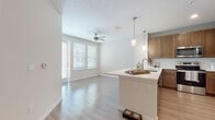 Located at 8500 Hunters Village Rd in Tampa, FL, this single-story residence offers a clean, contemporary design with light wood-style flooring that flows seamlessly throughout the entire space. The open-concept layout connects the kitchen and living area, creating a bright and airy atmosphere enhanced by natural light from multiple windows fitted with blinds and a ceiling fan overhead.

The kitchen is a standout feature, showcasing warm medium-toned cabinetry, a white countertop peninsula with pendant lighting above, a classic tile backsplash, and a full suite of stainless steel appliances including a refrigerator, range, and over-the-range microwave. Recessed lighting adds to the well-lit, functional workspace.

The bedroom is a comfortable, well-proportioned room with a ceiling fan, a window allowing natural light, and access to a generously sized walk-in closet outfitted with multi-tiered wire shelving systems for versatile storage organization.

The bathroom is elegantly appointed with a dual-sink vanity featuring rich wood cabinetry, white countertops, a wide mirror, and wood-style flooring that complements the rest of the home. A tub-shower combination with white tile surround completes the space. Overall, the residence presents a cohesive, modern aesthetic with neutral tones and quality finishes throughout.