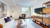 Located at 1200 S Grand Ave in Downtown Los Angeles, this thoughtfully designed one-bedroom, one-bathroom residence offers a modern and functional layout across a single floor. Wide-plank wood-style flooring flows throughout the main living areas, complemented by clean white walls and recessed lighting that create a bright, contemporary ambiance.

The open-concept kitchen is a standout feature, showcasing dark espresso cabinetry, a light mosaic tile backsplash, stainless steel appliances including a dishwasher, range, and microwave, and striking marble-style quartz countertops extending to a central island with bar seating. A dedicated dining area sits adjacent, offering a natural transition between kitchen and living spaces.

The living room benefits from large windows and a sliding glass door that open onto a private patio, inviting abundant natural light and views of lush greenery. The bedroom features plush carpeting, a window with outdoor views, and convenient access to two closets. The bathroom is finished with dark wood vanity cabinetry, subway tile tub surround, and wood-style flooring. An in-unit laundry closet with stacked washer and dryer adds everyday convenience. A dedicated entrance and hallway complete this well-organized residence.