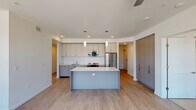 This contemporary single-floor residence is designed with a clean, modern aesthetic and a practical open layout. The kitchen serves as the heart of the home, showcasing flat-front cabinetry in a soft gray-beige tone, a white subway tile backsplash, and stainless steel appliances including a refrigerator and microwave. A spacious central island with a crisp white countertop provides ample prep space and casual seating, while pendant lighting adds a refined touch. Light wood-look flooring extends throughout the kitchen and living areas, contributing to a bright and cohesive atmosphere. The adjacent living area is open and airy, benefiting from recessed lighting and a seamless flow from the kitchen.

The bedrooms are finished with plush neutral carpeting and outfitted with ceiling fans for year-round comfort. Large windows flood the rooms with natural light and frame views of the surrounding landscape. The primary bedroom features dual windows offering expansive outdoor vistas.

Two full bathrooms are appointed with light wood flooring, gray cabinetry with white countertops, and tub-shower combinations. One bathroom includes built-in wall shelving for added storage convenience. The overall palette of whites, grays, and warm wood tones creates a calm, cohesive living environment throughout the space.