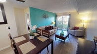 This single-floor residence offers a thoughtfully arranged layout that blends comfort and character throughout. The open-concept living and dining area serves as the heart of the home, featuring light wood-style flooring, a textured ceiling, and a striking teal accent wall adorned with a decorative metallic tree—creating a vibrant focal point. A sliding glass door floods the living room with natural light and provides access to a private balcony overlooking a landscaped outdoor area. The dining space flows seamlessly from the living room, accommodating a full dining set ideal for everyday meals or entertaining.

The galley-style kitchen is efficiently designed with white cabinetry, dark countertops, black appliances, and a stainless steel sink, all complemented by a window that brings in additional natural light. Both bedrooms are generously proportioned. The primary bedroom features a gray accent wall, mirrored closet doors that enhance the sense of space, and a window with outdoor views. The secondary bedroom is distinguished by a warm pink accent wall and ample natural light. A shared bathroom includes a tub-shower combination, a white vanity with dark countertop, and wood-style flooring, completing this well-appointed residence.