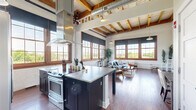 Located at 340 Rutgers St in Rochester's vibrant East End neighborhood, Unit 501 is a thoughtfully designed loft-style residence that blends industrial character with modern comfort. The single-floor layout offers a generous open-concept living and kitchen area bathed in natural light from large, wood-trimmed windows that frame treetop and cityscape views.

The living area showcases soaring ceilings with exposed wooden beams and industrial piping, complemented by rich hardwood floors that run throughout the space. White painted brick walls add texture and warmth, creating an inviting atmosphere ideal for both relaxing and entertaining.

The kitchen is a standout feature, centered around an oversized island with a concrete countertop and bar seating. Dark cabinetry pairs with stainless steel appliances, a deep farmhouse sink with subway tile backsplash, and a statement range hood — delivering a professional, chef-inspired aesthetic. Pendant lighting adds to the loft's industrial charm.

A dedicated workspace area provides a functional nook with ample wall space, while the bathroom offers a spa-like retreat with a wood-framed vanity, wide-format tile flooring, and a walk-in shower enclosed by sleek black-framed glass. Every detail of this unique space reflects a careful balance of urban edge and livable elegance.