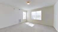 Located at 25 Flagstick Ln in Magnolia, Delaware, this single-floor unit offers a straightforward and functional layout designed for comfortable everyday living. The interior is finished with a neutral, light color palette throughout, creating a bright and airy atmosphere that feels open and welcoming.

The main living area is carpeted and well-lit, benefiting from multiple windows that allow generous natural light to fill the space. The windows provide views of the surrounding exterior, and their placement along adjacent walls ensures that sunlight reaches deep into the room at various times of day. The light-toned carpet complements the crisp white walls and ceiling, reinforcing the clean, understated aesthetic of the space.

Practical features are thoughtfully incorporated, including a wall-mounted HVAC unit for climate control, a ceiling light fixture, and standard electrical outlets positioned conveniently along the walls. The smooth white ceiling and clean wall surfaces lend the space a simple, move-in-ready appeal with minimal visual clutter.

Overall, this unit presents a tidy, well-maintained interior that emphasizes natural light, neutral finishes, and functional design — offering a solid foundation for personalization and comfortable day-to-day living.