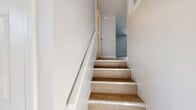 Located at 55 Merlino Dr in Groton, Connecticut, this thoughtfully updated three-floor home offers a clean, contemporary aesthetic with consistent finishes across every level. The kitchen is outfitted with white shaker-style cabinetry, black hardware accents, a neutral tile backsplash, light wood-look flooring, and a full suite of stainless steel appliances including a range, over-the-range microwave, and refrigerator. The main living areas feature light hardwood-style flooring and soft gray walls, creating a bright and airy atmosphere. A convenient half bath is found on one of the main levels, adding everyday practicality. The upper floor hosts a generously sized bedroom with plush gray carpet and a walk-in closet complete with a full-width hanging rod. A well-appointed full bathroom features warm wood-look flooring, a white shaker vanity, and a soaking tub with floor-to-ceiling tile surround and a built-in niche. Natural wood stair treads with white risers connect the floors, complementing the home's modern, cohesive design. The lower level includes a utility or storage space with epoxy-coated flooring, offering durable and functional square footage. Throughout, the home presents a move-in-ready condition with fresh finishes and a neutral palette.