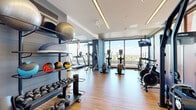 Located at 300 McRae Avenue in Ottawa, this well-appointed fitness center offers a comprehensive and thoughtfully designed workout environment across a single open floor. The space is characterized by its clean, contemporary aesthetic, featuring warm hardwood-style flooring, a mix of white and slate-blue accent walls, and a wood-paneled ceiling detail that adds a refined touch to the interior.

Floor-to-ceiling windows line multiple walls, flooding the facility with abundant natural light and providing expansive views of the surrounding Ottawa skyline and greenery — an energizing backdrop for any workout. Large-format motivational graphics are printed directly onto the windows, reinforcing the space's fitness-forward atmosphere.

The cardio zone is well-equipped with multiple treadmills, elliptical trainers, stationary bikes, and air bikes, all positioned to take advantage of the panoramic views. The strength training area offers a multi-station cable machine, adjustable benches, a full dumbbell rack, kettlebells, medicine balls, and stability balls neatly organized on a dedicated storage rack. Wall-mounted mirrors and mounted flat-screen TVs further enhance the training experience. Recessed and linear LED lighting ensures even illumination throughout. The result is a functional, modern fitness facility that balances performance and design seamlessly.